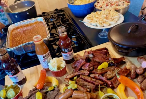 A spread of ribs, sausages, and sides on a cutting board